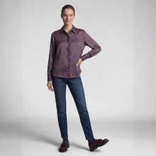 Load image into Gallery viewer, A woman modeling a long-sleeve button-up shirt with a small geometric pattern in purple and beige, paired with dark blue jeans and brown shoes, against a light gray studio background.
