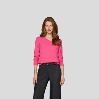 Woman wearing a pink sweater and dark pants on a light gray background