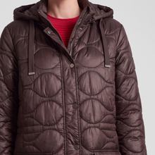 Load image into Gallery viewer, A close-up of a person wearing a dark brown quilted puffer jacket with a hood and drawstrings, layered over a red ribbed top, against a light gray background.
