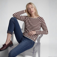 Load image into Gallery viewer, A woman sits on a clear acrylic chair wearing a long-sleeve crewneck sweater with dark red and beige horizontal stripes, blue jeans, and brown leather loafers against a light gray studio background.
