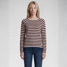 Load image into Gallery viewer, A woman modeling a long-sleeve knit top with horizontal burgundy and cream stripes, paired with dark blue jeans, against a light gray studio background.
