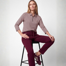 Load image into Gallery viewer, A woman sits on a black stool wearing a burgundy and white striped long-sleeve polo shirt and matching burgundy drawstring trousers, paired with burgundy sneakers with white stripes, against a light gray studio background.

