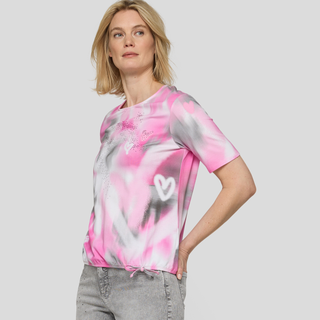 Woman wearing a pink and gray tie-dye shirt with a heart design on a plain background