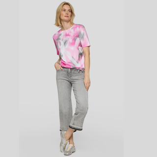 Woman wearing a pink tie-dye shirt and gray jeans on a light gray background