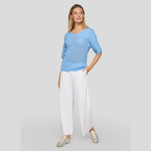 Load image into Gallery viewer, Woman wearing a light blue sweater and white pants on a gray background
