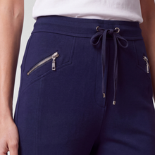 Load image into Gallery viewer, Close-up of navy blue drawstring sweatpants with zippered side pockets, worn with a white top against a light gray studio background.
