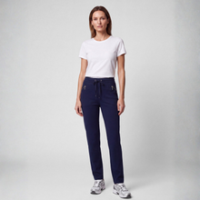 Load image into Gallery viewer, A woman modeling a pair of navy blue jogger-style pants with a drawstring waist and zippered side pockets, paired with a white t-shirt and gray sneakers, against a light gray studio background.
