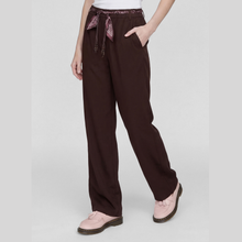 Load image into Gallery viewer, A person wearing dark brown wide-leg trousers with a patterned drawstring waistband, paired with light pink shoes, shown against a light gray studio background.
