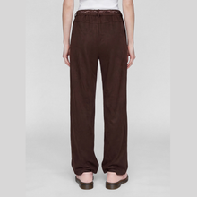 Load image into Gallery viewer, A person shown from the back wearing dark brown wide-leg pants with a lace-up waistband, paired with a white top and brown flat sandals, against a light gray studio background.
