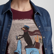 Load image into Gallery viewer, A close-up of a person wearing a graphic t-shirt under a blue denim shirt. The t-shirt features a burgundy crew neck and a large graphic print of a black dachshund wearing a blue beret and scarf, riding a light blue bicycle over a vintage book page background.
