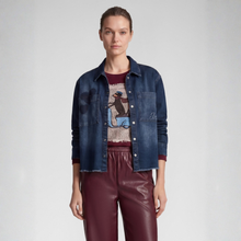 Load image into Gallery viewer, A model stands against a light gray studio background wearing a dark blue denim jacket over a graphic t-shirt and dark burgundy pants.
