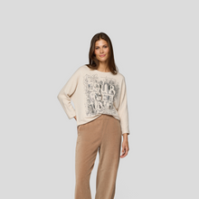 Load image into Gallery viewer, Woman wearing a beige sweater with text and brown pants on a light gray background
