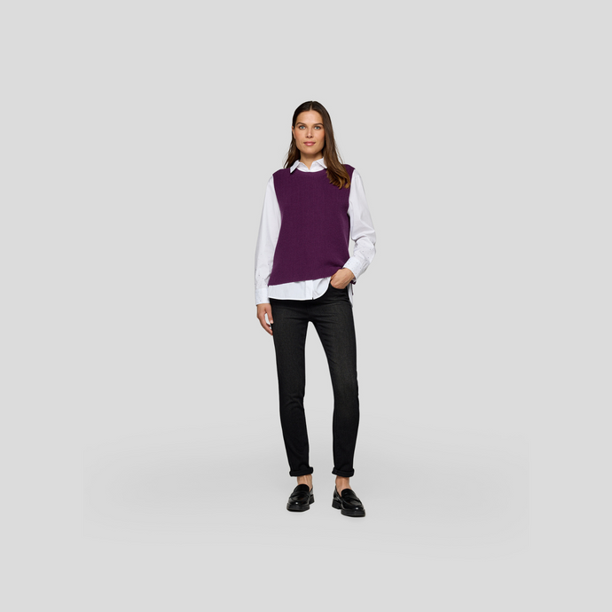 Woman wearing a purple sweater over a white shirt with black pants on a light gray background