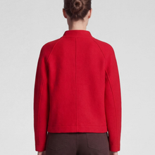 Load image into Gallery viewer, A model shown from the back wearing a bright red cropped jacket with a mock neck and raglan sleeves, paired with dark brown trousers, against a light gray studio background.
