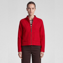 Load image into Gallery viewer, A woman modeling a bright red cropped zip-up jacket with two front patch pockets, worn over a striped top and dark brown trousers, against a light gray studio background.
