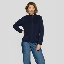 Load image into Gallery viewer, A woman modeling a navy blue ribbed zip-up jacket with a stand collar and front pockets, paired with blue jeans, against a light gray studio background.
