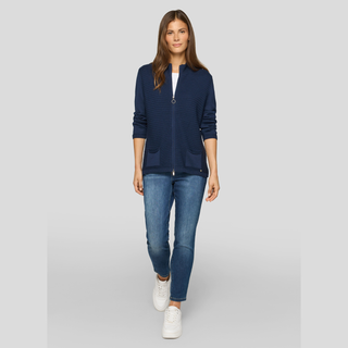 Woman wearing a navy cardigan, white shirt, blue jeans, and white sneakers on a light gray background