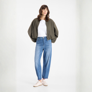 Woman wearing a green cardigan, white shirt, and blue jeans on a white background