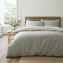 Load image into Gallery viewer, A neatly made bed in a bright bedroom with a striped duvet cover and matching pillow shams in a muted sage green and off-white, styled with a wooden headboard, side table, and window.
