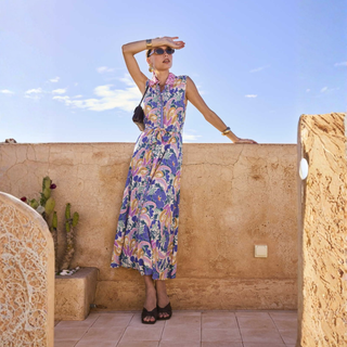Woman in a floral dress standing on a rooftop with a clear blue sky.