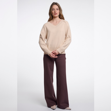 Load image into Gallery viewer, A woman modeling a beige long-sleeve knit sweater and dark brown wide-leg trousers against a light gray studio background.
