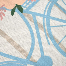 Load image into Gallery viewer, A close-up of a woven textile pattern featuring a bicycle design in light blue, with beige outlines, a peach background, and a small green leaf accent.
