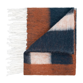 A Scatterbox throw folded with tones of copper, black and cream and thick white fringe along the side