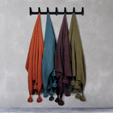 Load image into Gallery viewer, Four Scatterbox throws hanging on a grey wall from black hooks, featuring orange, blue, aubergine and green
