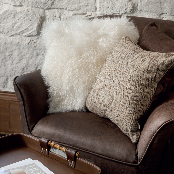 Promo shot of the Inish Murray cushion on a brown leather chair and a fluffy white cushion