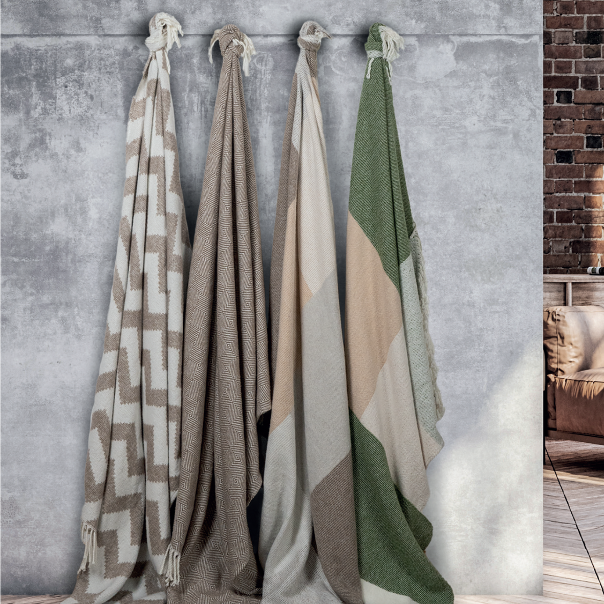 Four Scatterbox throws hanging on a grey wall with different shades of cream, brown, beige and green