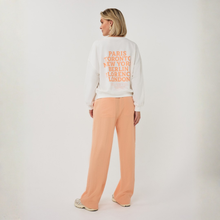 Load image into Gallery viewer, Person wearing a white sweatshirt with city names and peach pants on a white background
