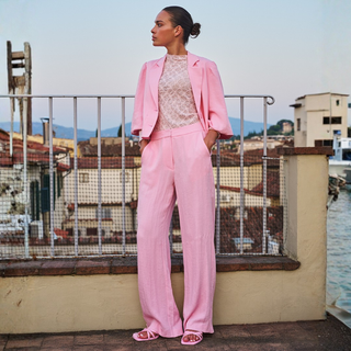 Woman in a pink suit standing on a rooftop with a scenic background