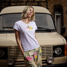 Load image into Gallery viewer, Woman wearing a white t-shirt with a floral design in front of a beige van.
