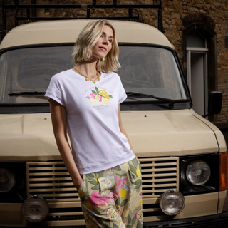 Woman wearing a white t-shirt with a floral design in front of a beige van.