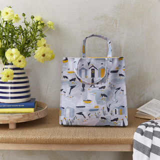 Tote bag with animal pattern on a wooden surface next to a vase with flowers and books.