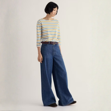 Load image into Gallery viewer, A woman modeling a three-quarter sleeve striped top with yellow, white, and blue horizontal stripes, paired with wide-leg blue jeans and a brown belt, against a plain off-white studio background.
