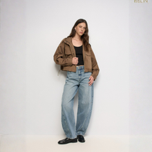 Load image into Gallery viewer, A model stands against a plain white studio background wearing a brown cropped jacket over a black top, light-wash wide-leg jeans, and black loafers. The brand name 'ABSLIN' appears in the top right corner.

