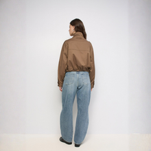 Load image into Gallery viewer, A woman viewed from behind wearing a brown cropped jacket and wide-leg light blue jeans, standing against a plain light gray studio background.
