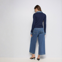Load image into Gallery viewer, A woman shown from the back wearing a navy blue ribbed knit long-sleeve top, wide-leg cropped blue jeans, and black heeled sandals against a plain light gray studio background.
