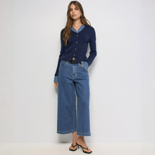 Load image into Gallery viewer, A woman modeling a navy blue ribbed button-front cardigan with a light blue collar detail, paired with wide-leg blue jeans and black sandals, against a plain white studio background.
