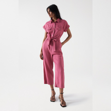 Load image into Gallery viewer, Model is wearing Salsa jumpsuit in Old pink color. Holding her one hand in a side pocket. Jumpsuit is straight cropped leg trousers with buttoned top. Has collar and short sleeves.
