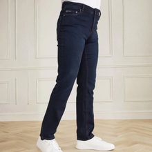 Load image into Gallery viewer, Person wearing dark blue jeans and white sneakers against a light-colored paneled wall.
