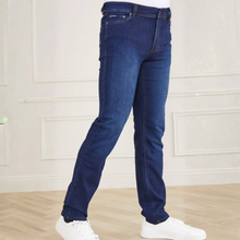 Load image into Gallery viewer, Blue jeans worn by a person on a light wooden floor with a white paneled wall background
