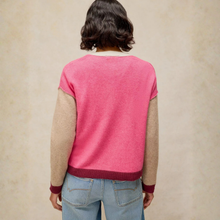 Load image into Gallery viewer, A person shown from the back wearing a color-block knit sweater with a bright pink body, beige sleeves, and dark red ribbed trim, paired with light blue jeans against a textured beige studio background.
