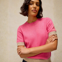 Load image into Gallery viewer, A woman wearing a bright pink short-sleeve knit sweater with beige ribbed trim at the cuffs and hem, posed against a neutral beige textured background.
