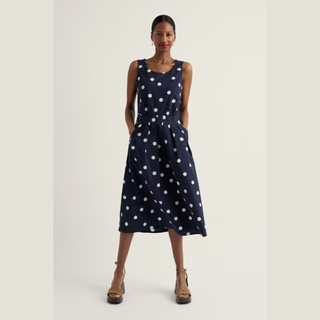 Woman wearing a navy dress with white polka dots on a light gray background
