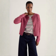 Load image into Gallery viewer, A model wearing a fuzzy pink cropped cardigan over a red and white striped t-shirt, paired with dark blue wide-leg jeans, against a plain off-white background.
