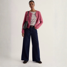 Load image into Gallery viewer, A model stands against a plain light background wearing a fuzzy pink cardigan over a black and white striped shirt, paired with dark wide-leg jeans, a brown belt, and a black shoulder bag.
