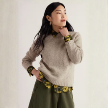 Load image into Gallery viewer, A woman wearing a beige knit sweater over a yellow and green floral collared shirt and olive green pants, posing against a plain off-white background.
