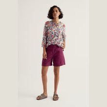 Load image into Gallery viewer, Woman wearing a floral blouse and purple shorts on a plain background
